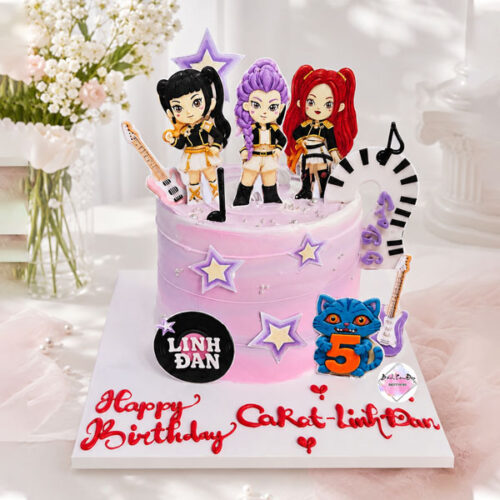 Bánh kem BabyMonster màu hồng trang trí mô hình nhóm nhạc, đàn guitar, phím đàn piano và nốt nhạc dành cho bé gái.